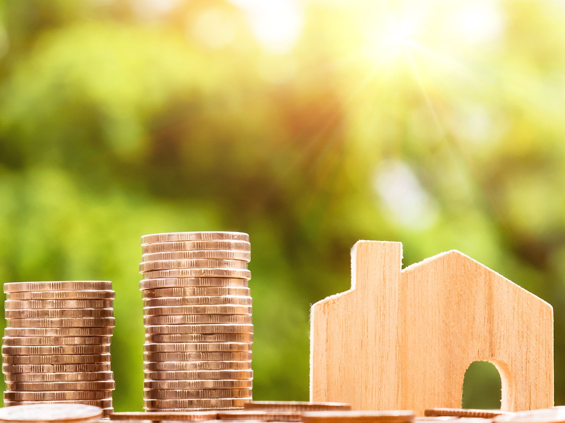 Des pièces de monnaie empilées à côté d'une petite maison découpée dans une planche de bois